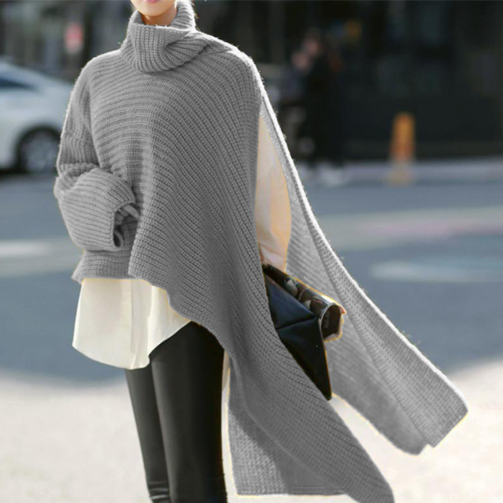 Grijze gebreide poncho met col, gedragen over witte blouse en zwarte broek. Modieuze herfst- of winteroutfit voor dames, casual en stijlvol.