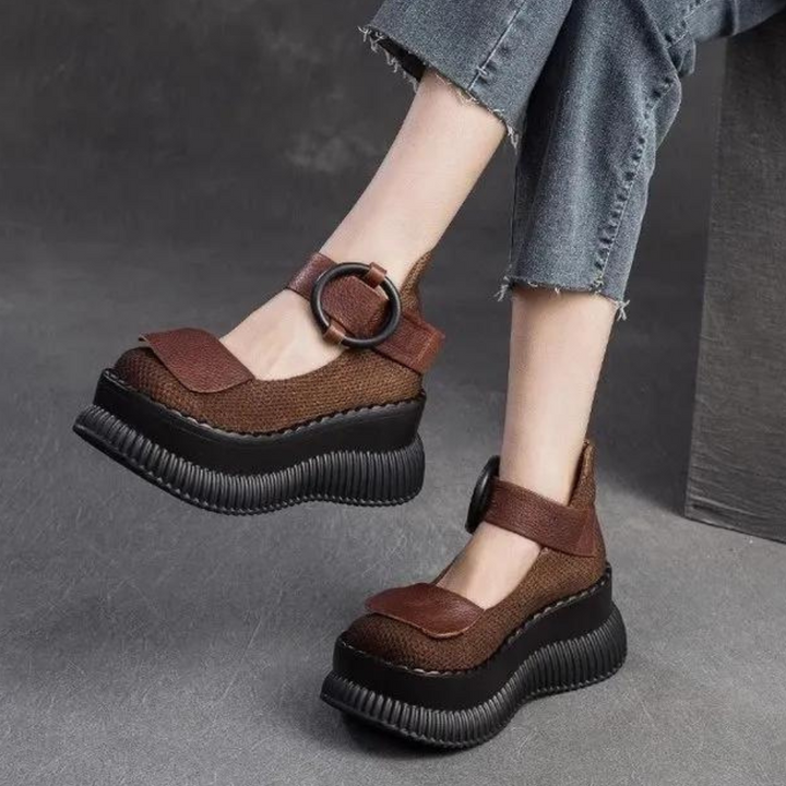 Bruine damesplatformschoenen met dikke zwarte zolen en verstelbare riem, gedragen met opgerolde spijkerbroek. Modieuze en comfortabele damesschoenen.