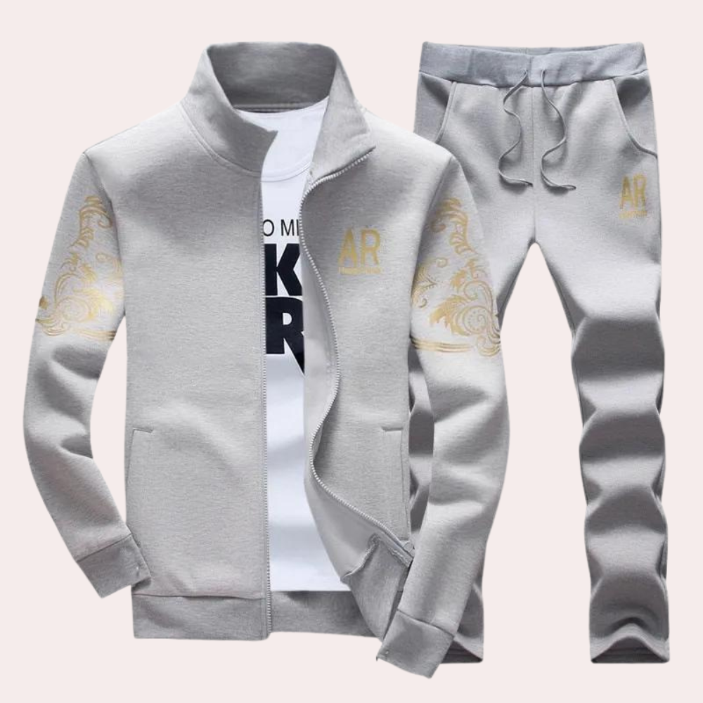 Grijs trainingspak voor heren met gouden details, inclusief jas en joggingbroek. Comfortabel sportkledingontwerp, ideaal voor casual en fitness.