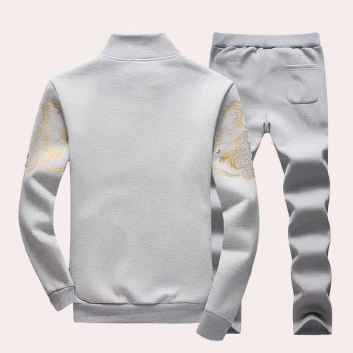 Grijze trainingspak set met gouden details op de mouwen, bestaande uit een sweatshirt en joggingbroek. Comfortabele sportkleding voor heren.