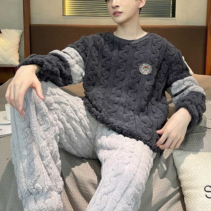 Jonge man in comfortabele, grijze fleece pyjama met kabelpatroon, zittend op een bank. Ideaal voor wintermode en huiselijke gezelligheid.