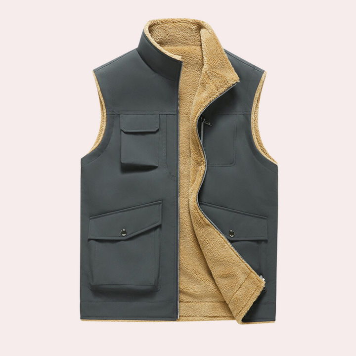 Grijze herenvest met opstaande kraag en beige fleecevoering, meerdere zakken, ideaal voor outdooractiviteiten. Comfortabele en warme bodywarmer.
