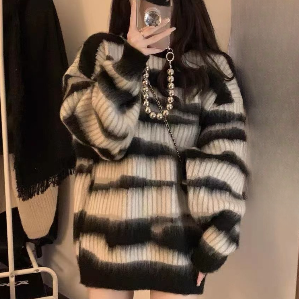 Zwarte en witte gestreepte oversized trui, gedragen door een vrouw, met een opvallende parelketting. Modieuze winterkleding, trendy damesmode.