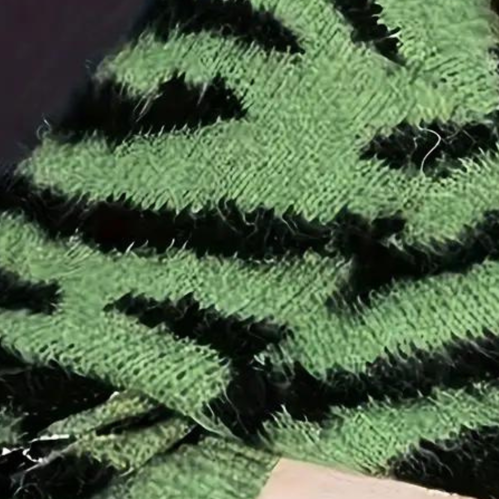 Groene gebreide stof met zwarte zigzagpatronen, close-up. Textieltextuur, modeontwerp, breiwerkdetails.