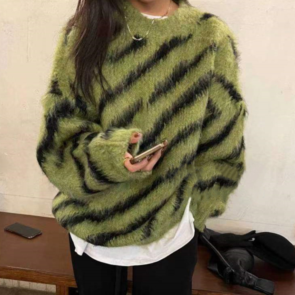 Vrouw in groene, gestreepte trui met zwarte diagonale strepen, houdt smartphone vast. Modieuze winterkleding, casual stijl, trendy outfit.