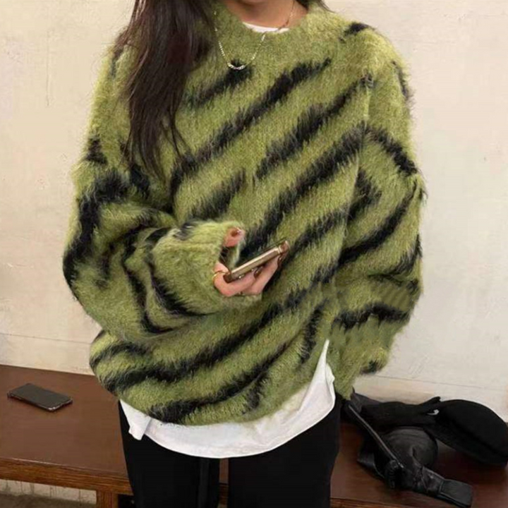 Vrouw in groene, gestreepte trui met zwarte diagonale strepen, houdt smartphone vast. Modieuze winterkleding, casual stijl, trendy outfit.