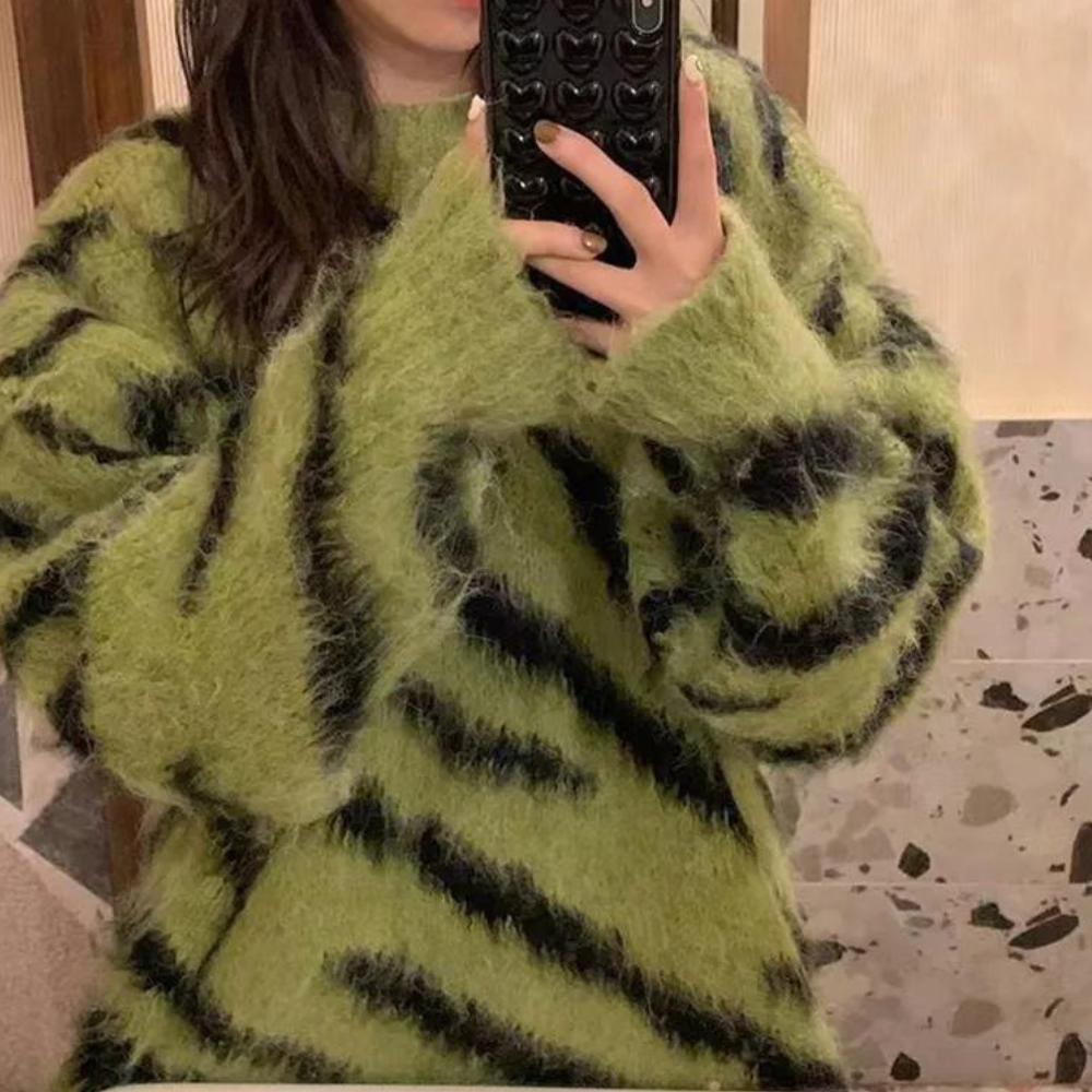 Groene trui met zwarte strepen, gedragen door persoon die een telefoon met hartjeshoes vasthoudt. Modieuze, pluizige damestrui, herfstkleding.