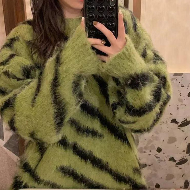 Groene trui met zwarte strepen, gedragen door persoon die een telefoon met hartjeshoes vasthoudt. Modieuze, pluizige damestrui, herfstkleding.