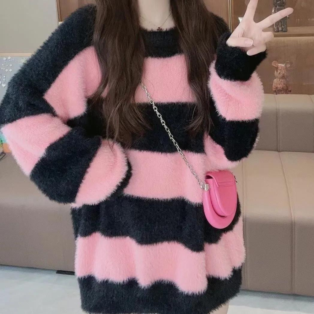 Vrouw in roze-zwarte gestreepte trui met roze schoudertas, maakt vredesteken. Trendy wintermode, comfortabele oversized stijl.
