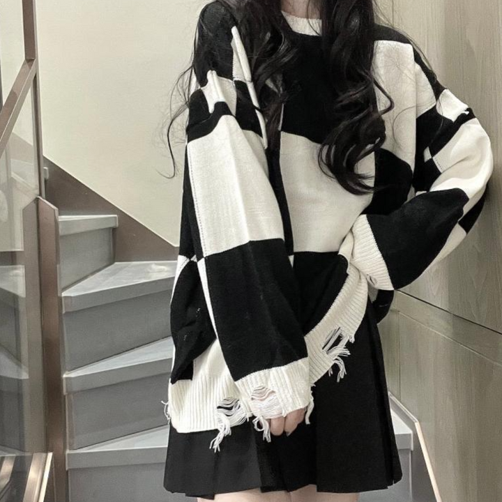 Zwart-witte oversized trui met gerafelde details, gedragen door vrouw op trap. Modieuze streetwear, casual stijl, trendy kleding.