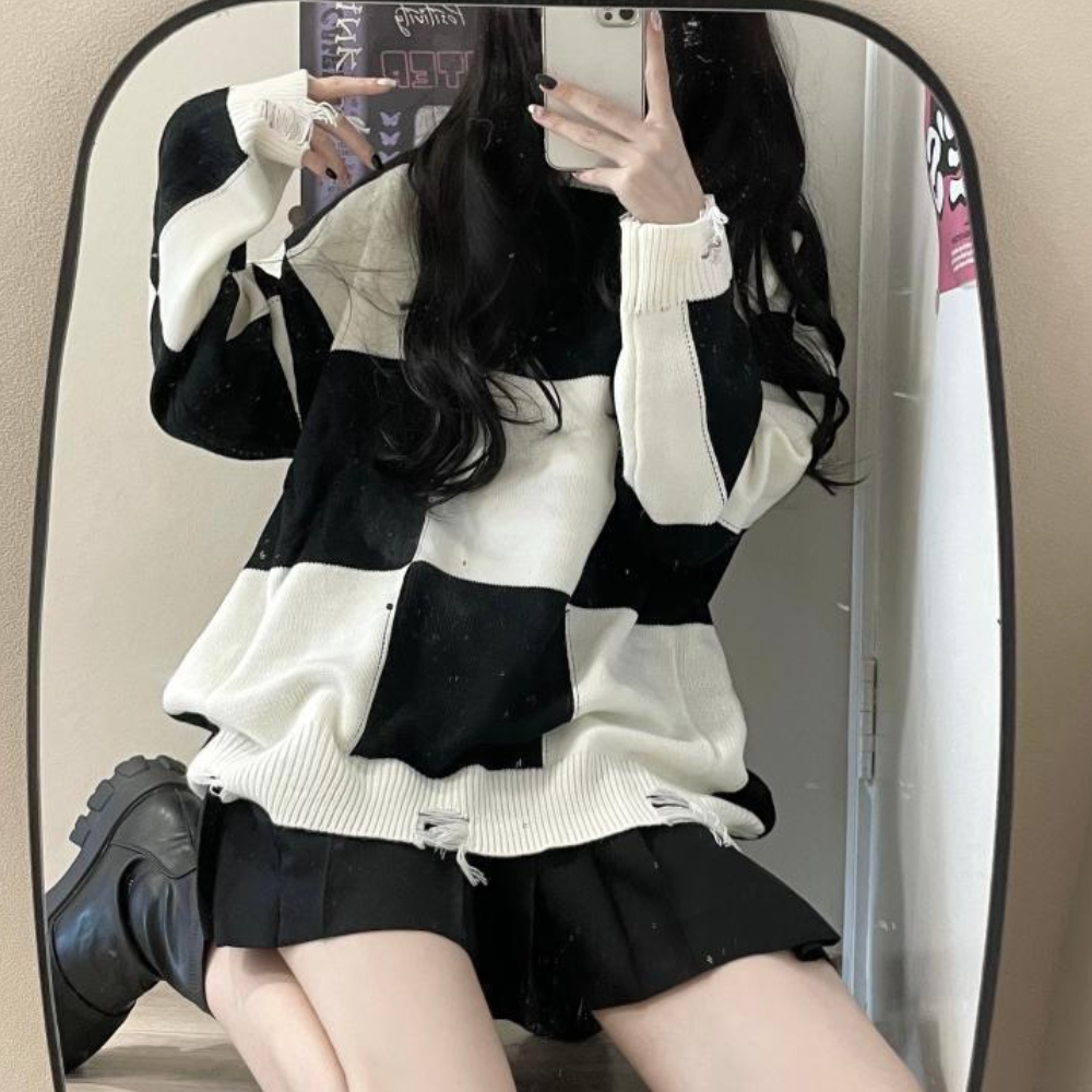 Vrouw in oversized zwart-wit geruite trui, zwarte rok en laarzen, poseert voor spiegel. Modieuze herfstoutfit, casual streetwear stijl.