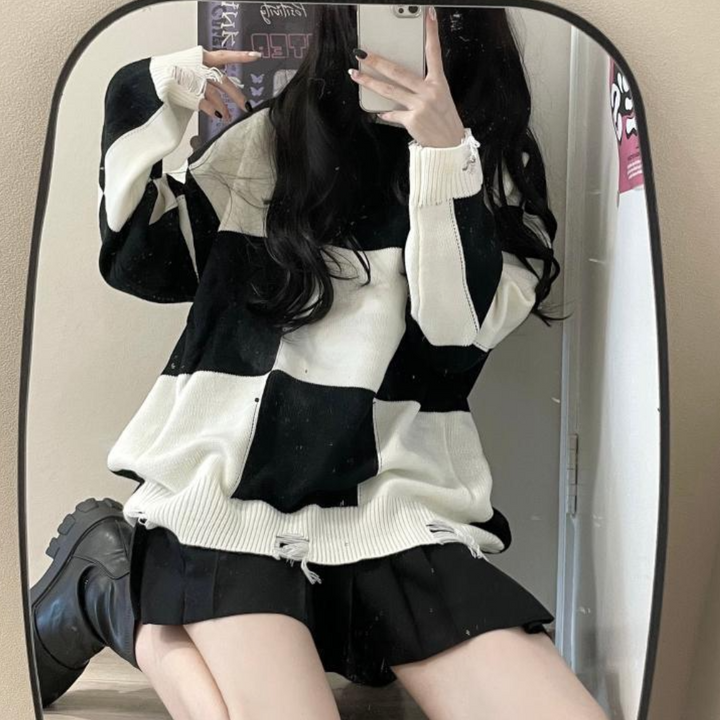 Vrouw in oversized zwart-wit geruite trui, zwarte rok en laarzen, poseert voor spiegel. Modieuze herfstoutfit, casual streetwear stijl.