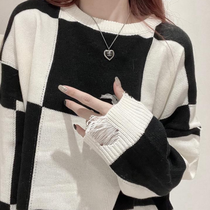 Zwart-witte geruite trui met hartvormige hanger, gedragen door persoon met lange nagels. Modieuze dameskleding, trendy herfststijl.