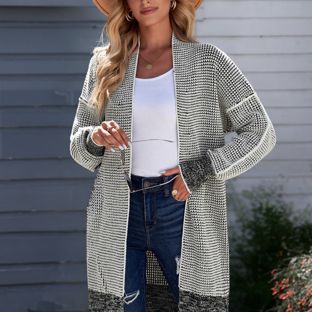 Vrouw draagt gebreid vest in grijs-wit patroon, gecombineerd met een witte top en blauwe jeans. Perfecte herfstmode, casual en stijlvol.