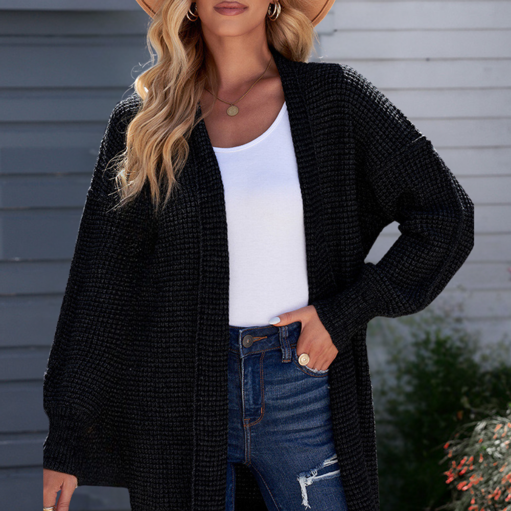 Vrouw in zwarte gebreide cardigan, witte top en blauwe jeans, poseert buiten. Mode, herfstkleding, casual stijl, damesmode, trendy outfit.
