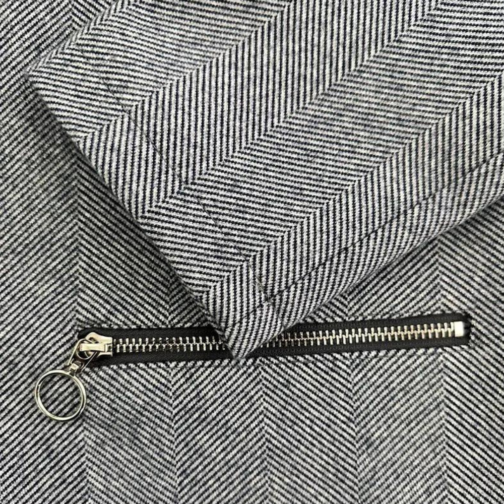 Grijze visgraatstof met metalen ritssluiting en ringtrekker, detailopname. Perfect voor modeontwerp, textiel en kledingproductie.
