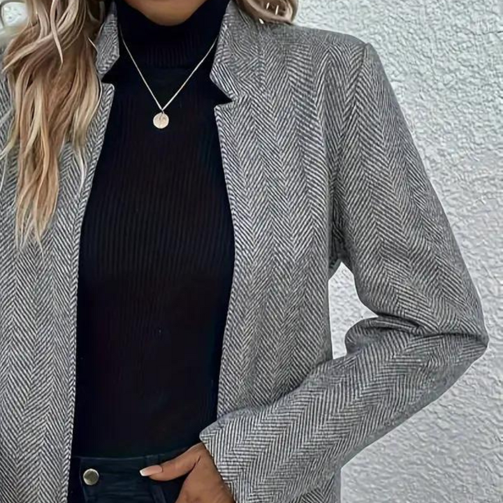 Grijze visgraat blazer voor dames, gecombineerd met zwarte coltrui en ketting. Stijlvolle zakelijke outfit, herfstmode 2023.
