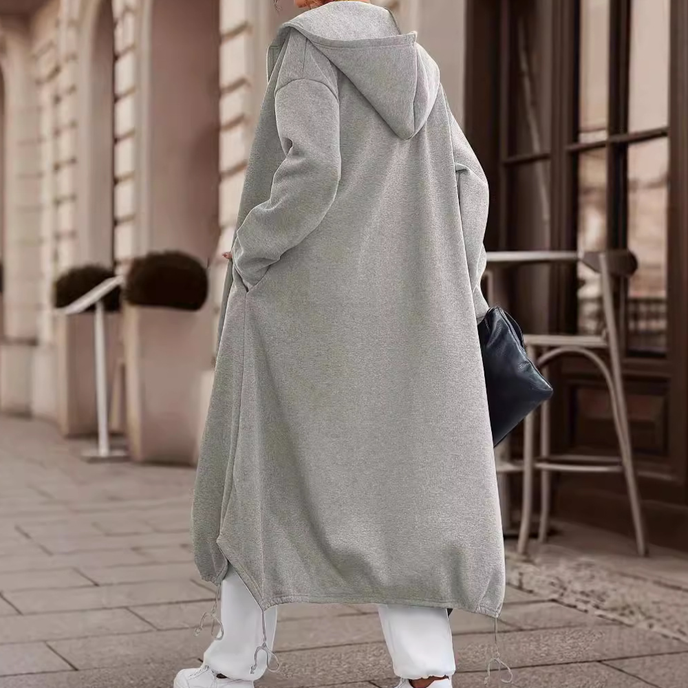 Grijze lange hoodie jas voor dames, casual streetwear stijl, met capuchon en zakken, perfect voor herfstmode. Comfortabele en trendy outfit.
