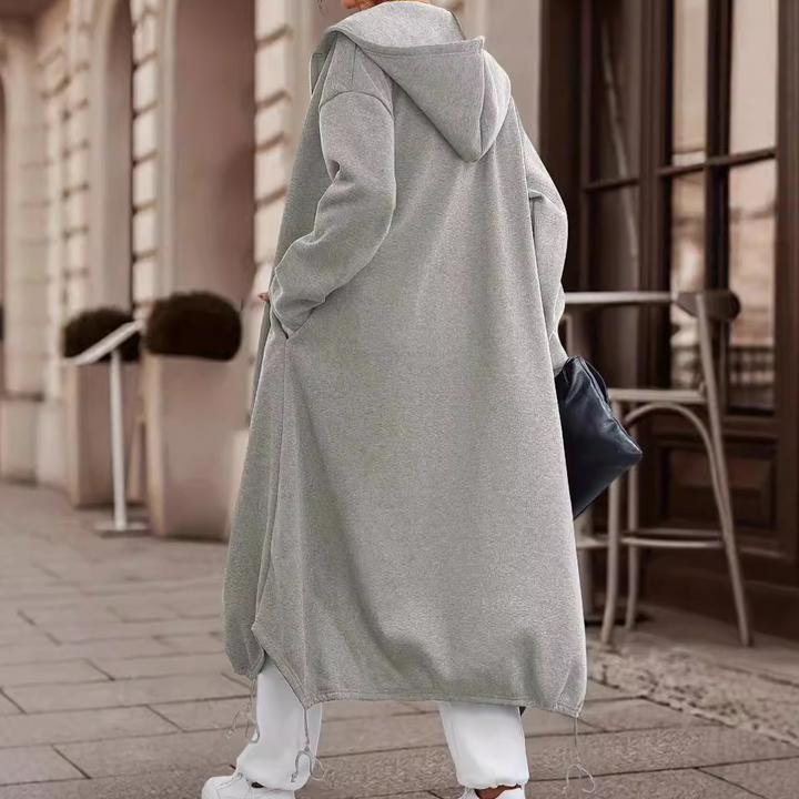 Grijze lange hoodie jas voor dames, casual streetwear stijl, met capuchon en zakken, perfect voor herfstmode. Comfortabele en trendy outfit.