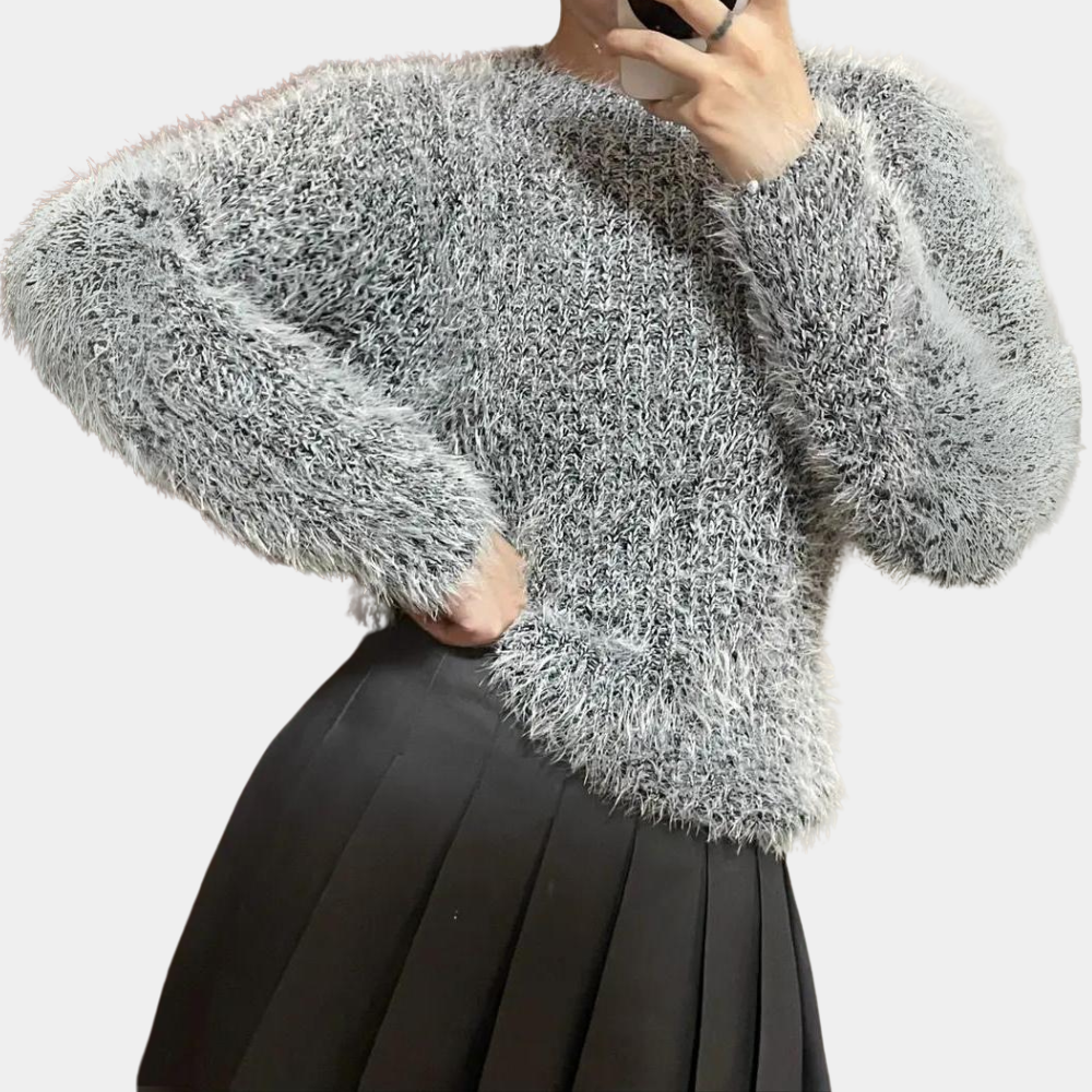 Grijze pluizige trui met lange mouwen, gedragen door persoon, gecombineerd met zwarte geplooide rok. Modieuze winterkleding, trendy damesmode.