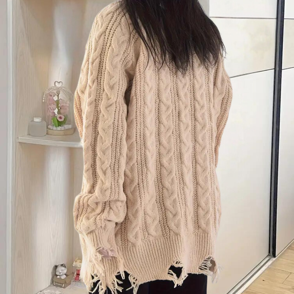 Vrouw draagt beige kabeltrui met gerafelde zoom, trendy oversized stijl. Perfect voor herfstmode, casual en comfortabel.