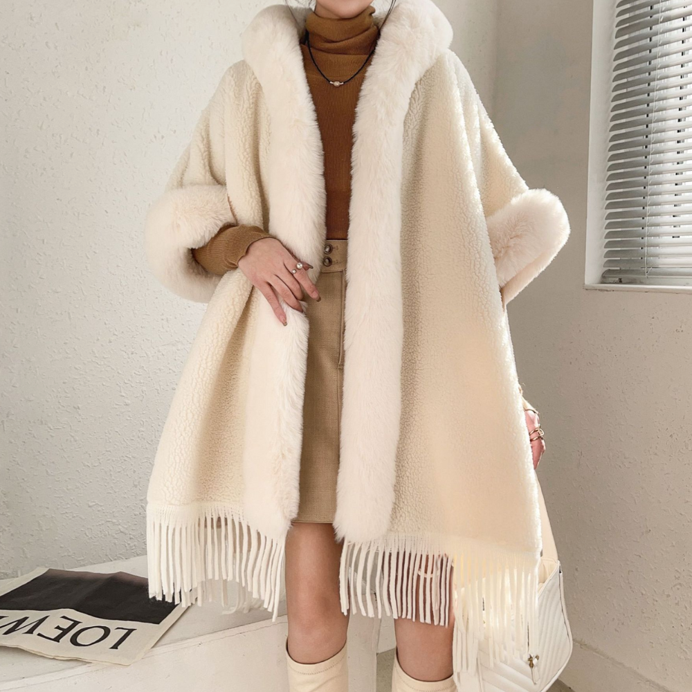 Vrouw in stijlvolle beige wollen jas met witte bontkraag en franjes, gecombineerd met bruine trui en rok. Wintermode, trendy dameskleding.