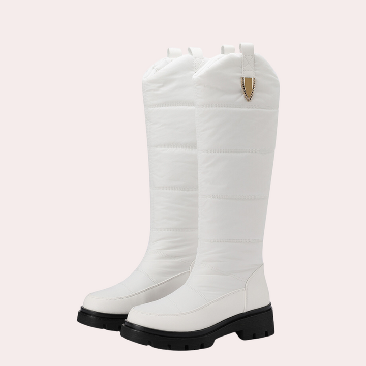 Witte kniehoge laarzen met dikke zwarte zool, gewatteerd ontwerp en gouden detail. Modieuze winterlaarzen voor dames, ideaal voor koude seizoenen.