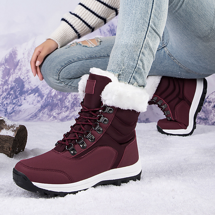 Vrouw met gebreide trui en gescheurde jeans draagt bordeauxrode winterlaarzen met witte bontkraag, ideaal voor sneeuw en koude weersomstandigheden.