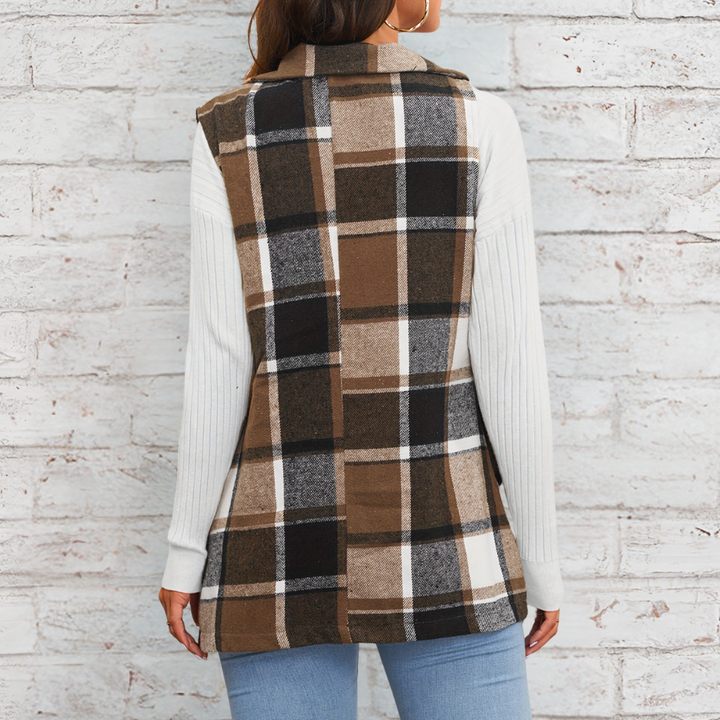 Vrouw draagt geruite bruine en zwarte vest met witte mouwen, tegen bakstenen muur. Modieuze dameskleding, herfststijl, casual outfit.