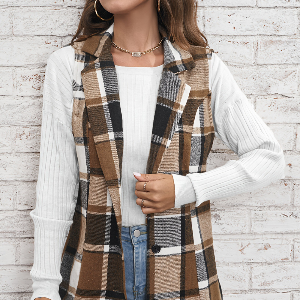 Vrouw draagt geruite bruine en zwarte lange gilet over witte trui, casual herfstmode, trendy dameskleding, stijlvolle outfit tegen bakstenen muur.