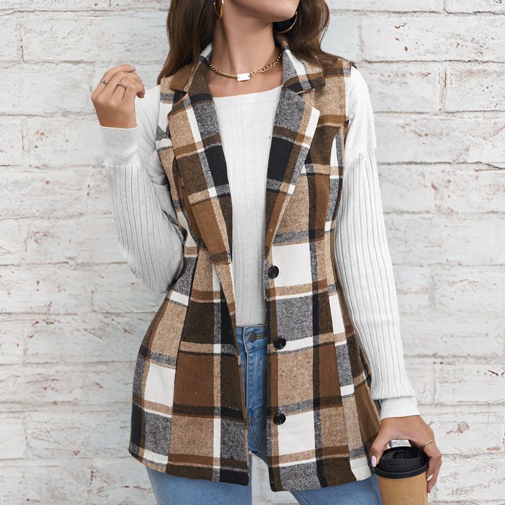 Vrouw in geruite bruine blazer, witte trui en blauwe jeans tegen bakstenen muur, houdt koffiebeker vast. Modieuze herfstoutfit, casual stijl.