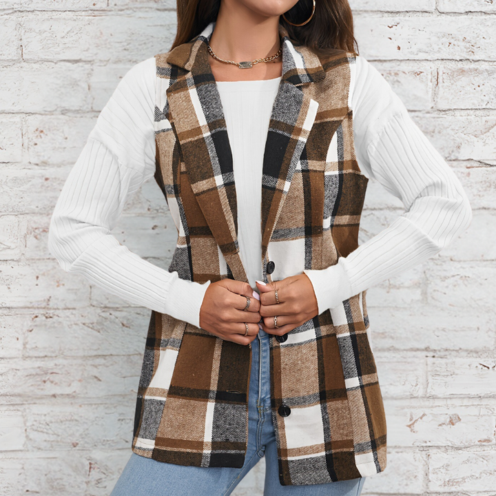 Vrouw draagt geruite bruine blazer met witte trui en spijkerbroek, tegen bakstenen muur. Modieuze dameskleding, herfststijl, casual outfit.