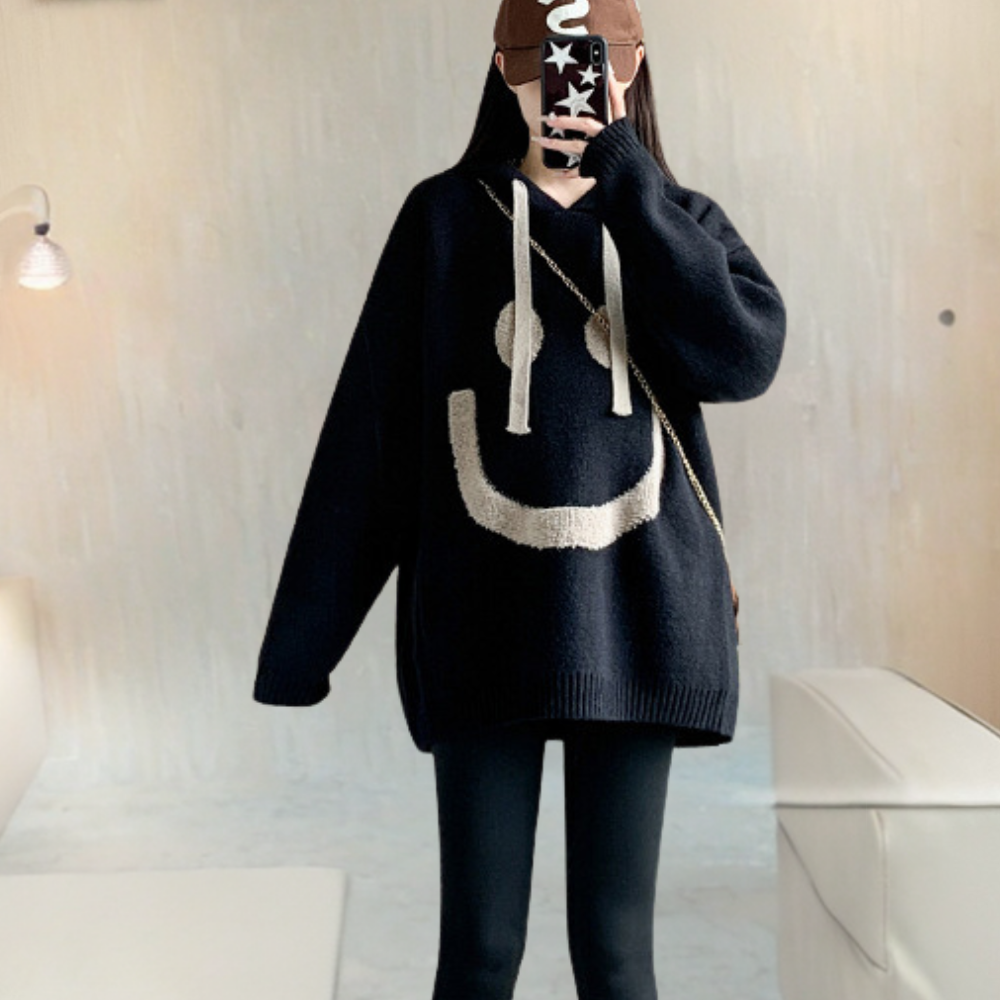 Zwarte oversized trui met grote smileyprint, gedragen door persoon met zwarte legging. Trendy casual mode, comfortabele herfst- en winterkleding.