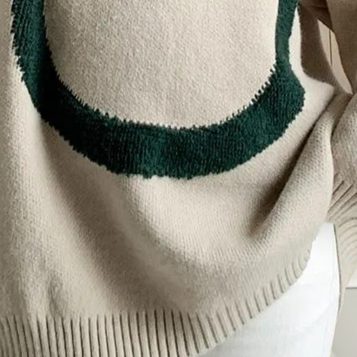 Beige trui met groene geborduurde cirkel, close-up. Modieuze dameskleding, herfstcollectie, zachte stof, casual stijl.