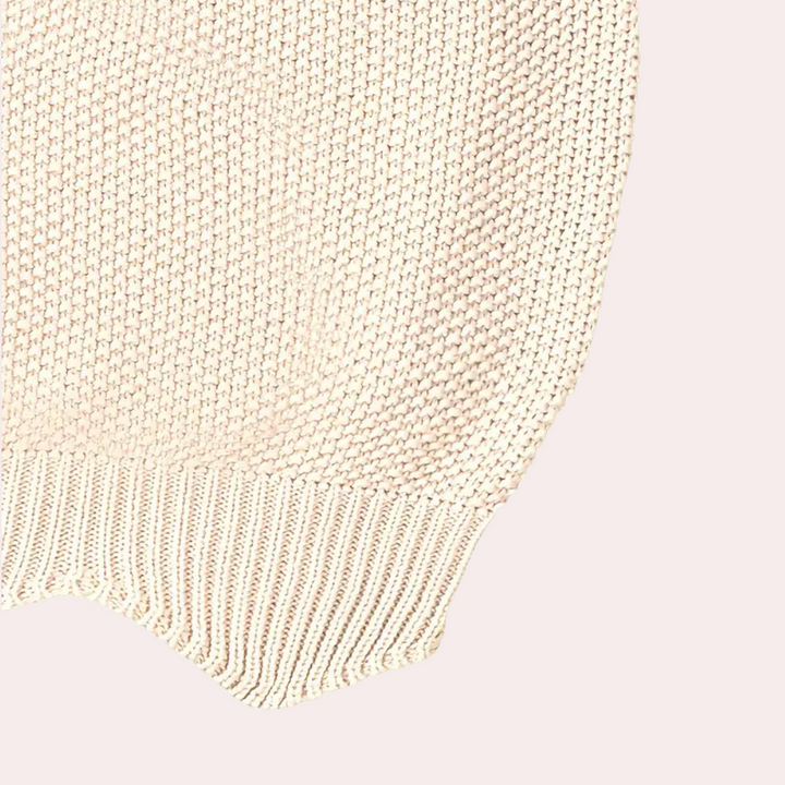 Beige gebreide trui detail, close-up van textuur en patroon. Zachte katoenen stof, modieus en comfortabel. Perfect voor casual herfst- en winteroutfits.