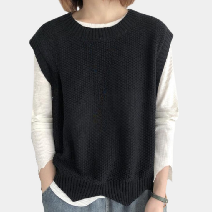 Zwarte gebreide damestrui zonder mouwen, gedragen over een witte longsleeve. Modieuze casual outfit, ideaal voor herfst- en winterlagen.