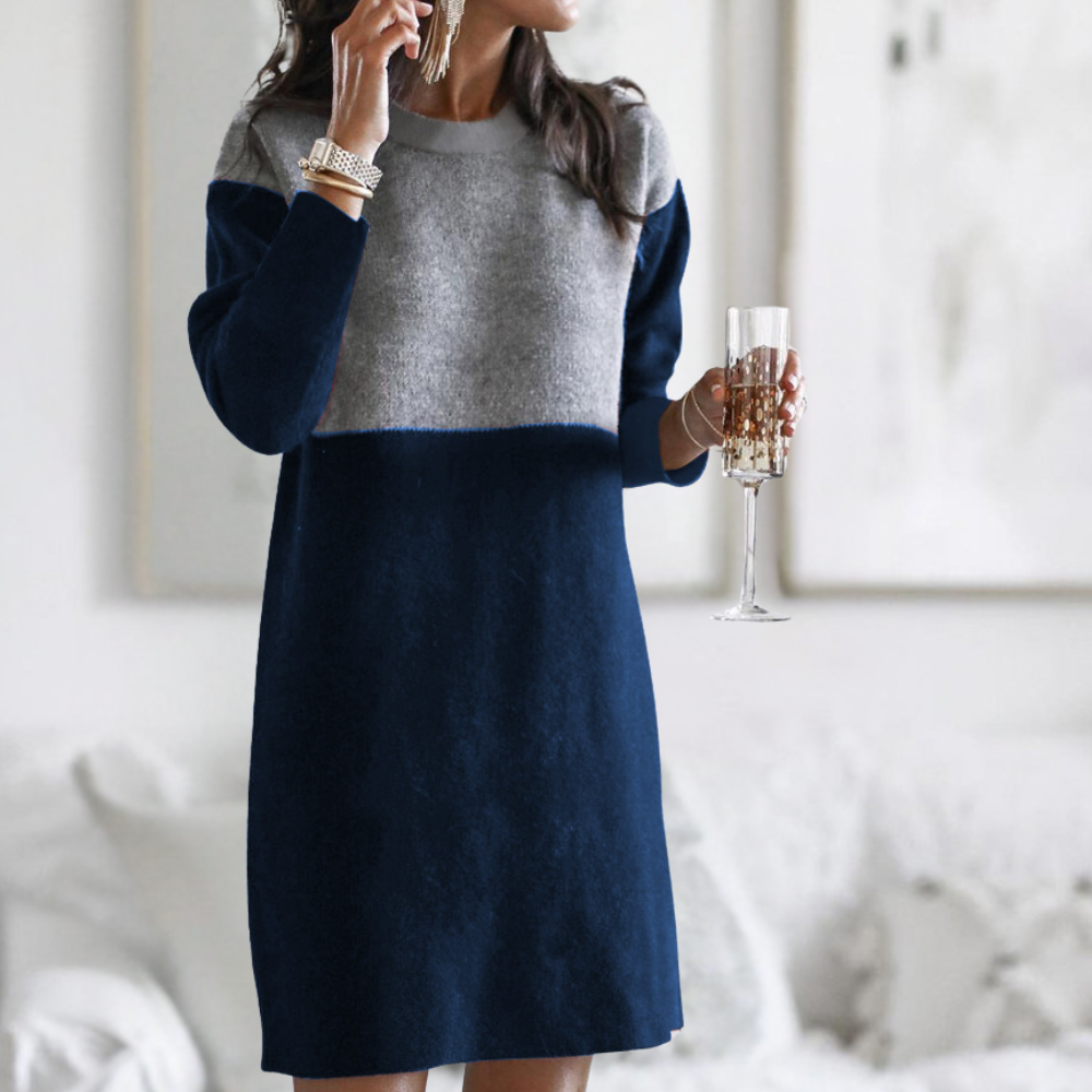 Vrouw in stijlvolle, tweekleurige trui-jurk in marineblauw en grijs, met champagneglas. Modieuze dameskleding, herfst-winter outfit.