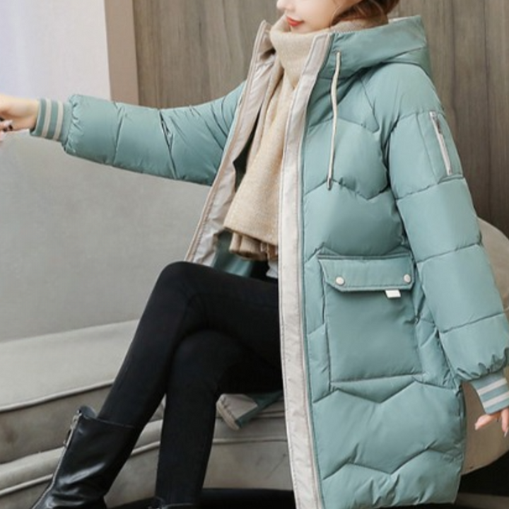 Vrouw in lichtgroene gewatteerde winterjas met capuchon, zittend op bank. Modieuze damesjas, warme winterkleding, trendy buitenkleding.