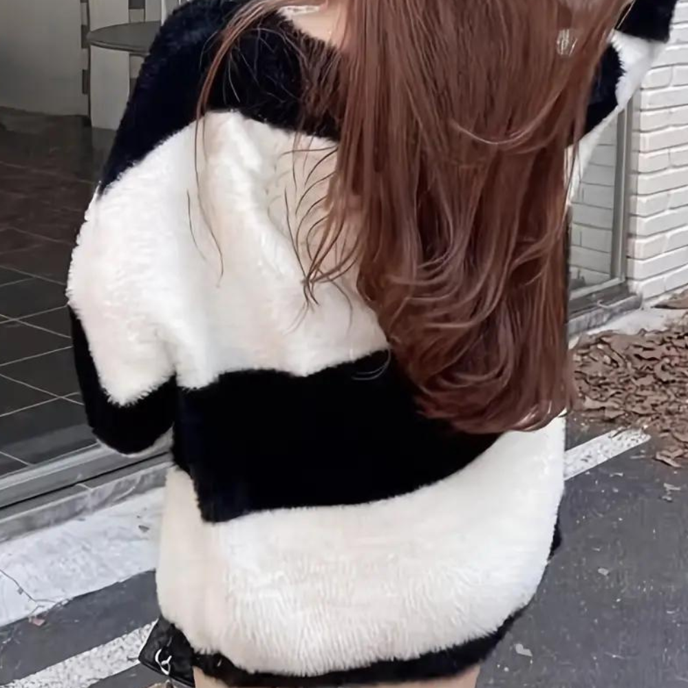 Vrouw in zwart-witte gestreepte trui met lange bruine haren, buiten bij een gebouw. Modieuze winterkleding, casual stijl, trendy outfit.