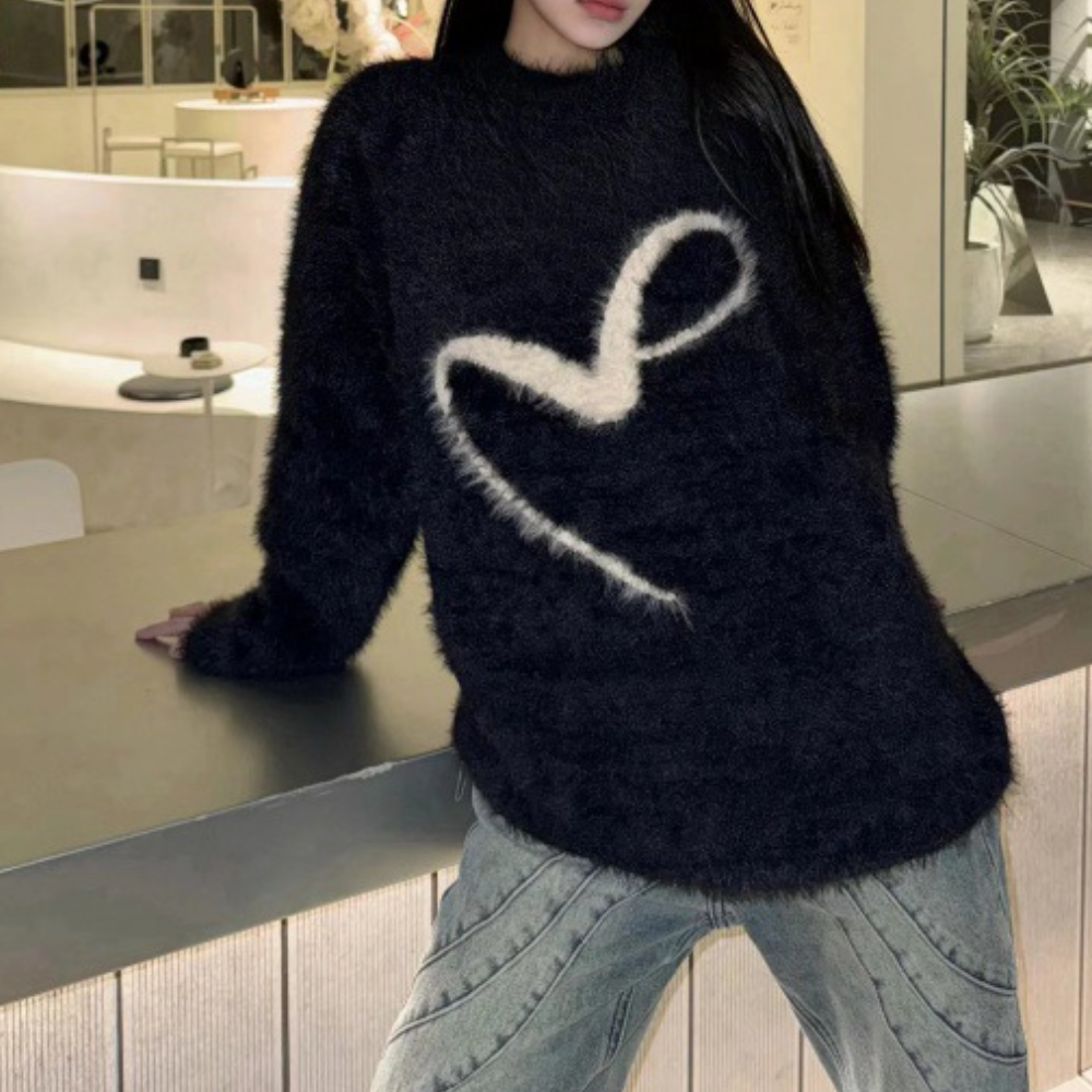 Vrouw in zwarte, pluizige trui met wit hartpatroon, leunend op moderne toonbank. Modieuze casual outfit, trendy winterkleding.