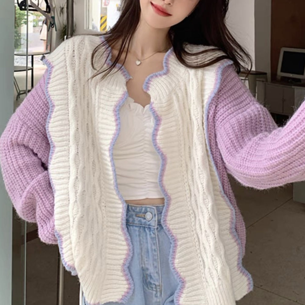 Vrouw draagt gebreid vest met kabelpatroon, witte en paarse tinten, trendy mode, casual stijl, perfect voor herfst en winter.