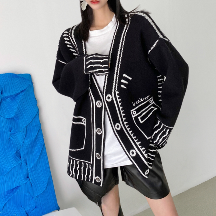 Vrouw draagt zwarte oversized cardigan met witte stiksels en knopen, gecombineerd met wit T-shirt en zwarte leren rok. Modieuze herfstkleding.