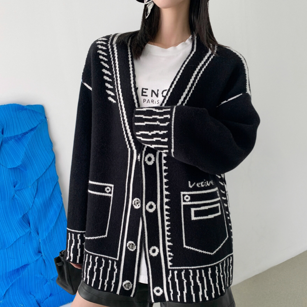 Vrouw draagt zwarte oversized cardigan met witte strepen en knopen, gecombineerd met een witte T-shirt en zwarte rok. Trendy damesmode, herfstkleding.
