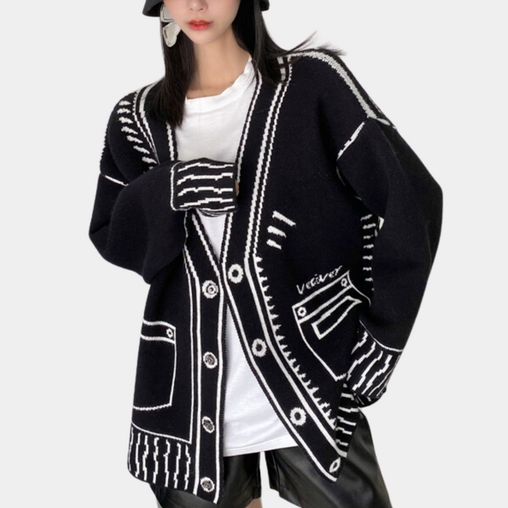 Zwarte oversized cardigan met witte grafische patronen, gedragen door model. Trendy damesmode, comfortabele pasvorm, geschikt voor casual outfits.