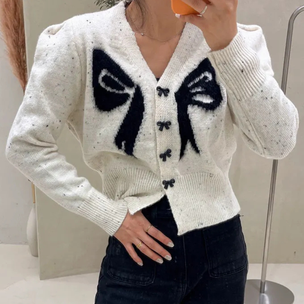 Witte gebreide cardigan met zwarte strikmotief, lange mouwen en knoopsluiting, gedragen door model. Trendy damesmode, herfst-winter kledingstijl.