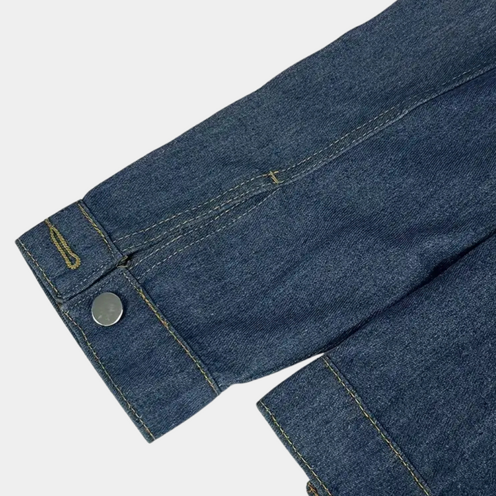 Denim jas detail met metalen knoop en stiksels, blauwe spijkerstof, modieuze kleding, close-up mouw, casual stijl, hoogwaardige afwerking.