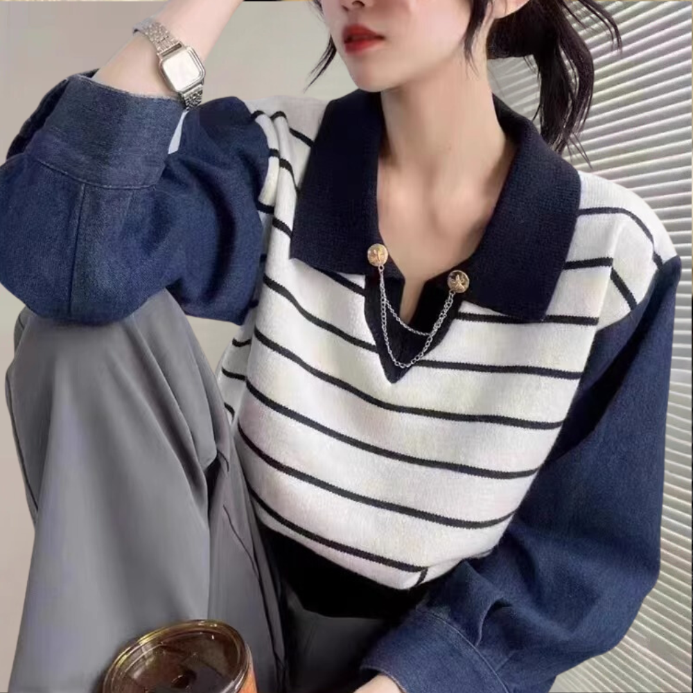 Vrouw draagt gestreepte trui met donkerblauwe kraag en mouwen, zilveren horloge, grijze broek. Modieuze dameskleding, casual stijl.