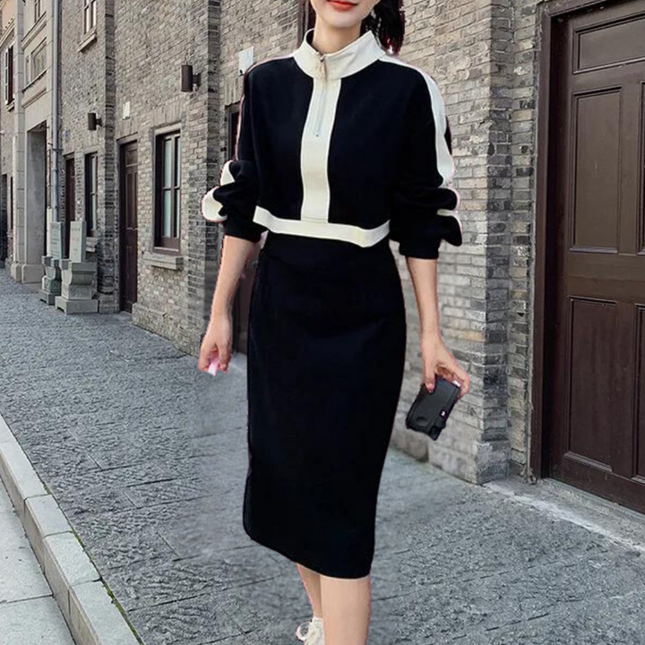 Vrouw in stijlvolle zwarte jurk met witte strepen, wandelend op een stenen trottoir. Elegante mode, stedelijke achtergrond, casual chic outfit.