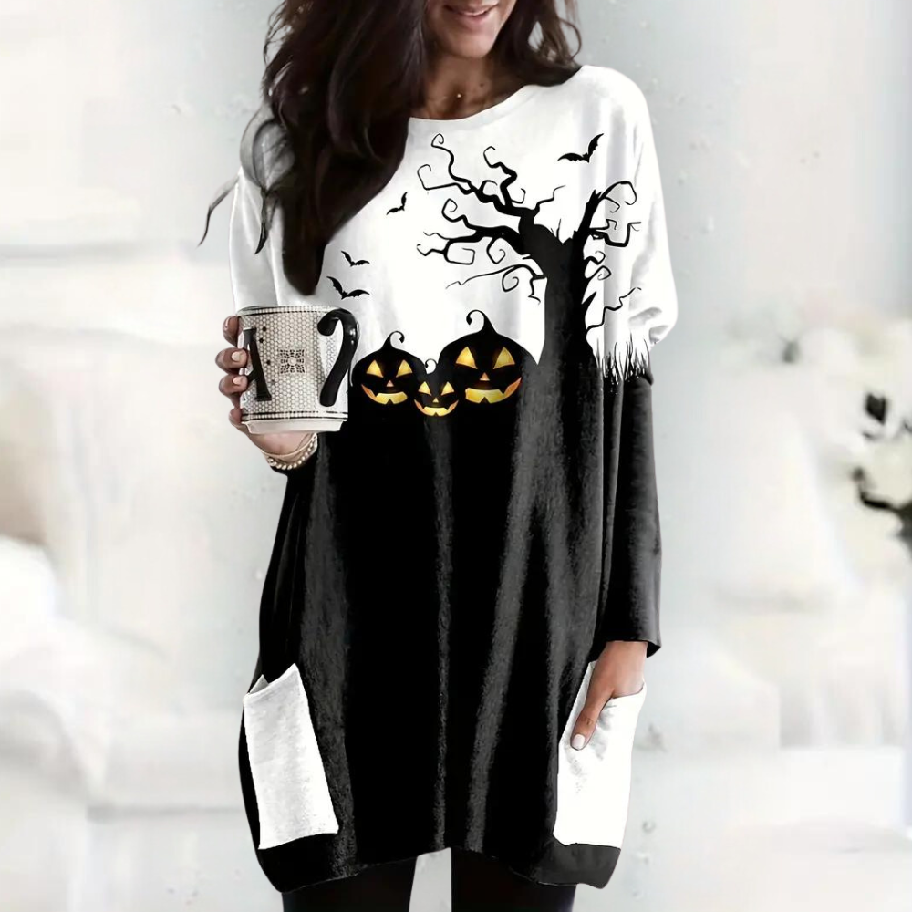 Vrouw draagt Halloween-trui met pompoenen, boom en vleermuizen, houdt mok vast. Perfect voor herfstmode en Halloween-thema.