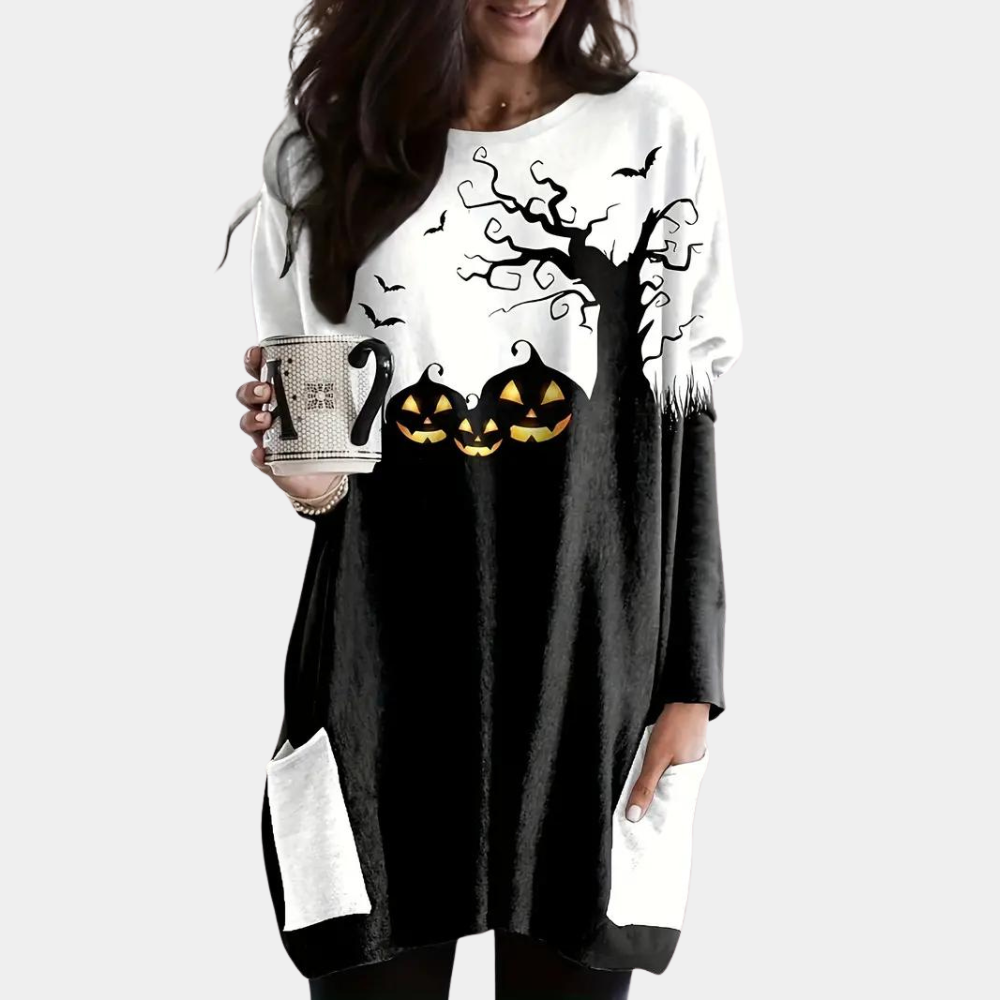 Vrouw draagt Halloween-trui met pompoenen, boom en vleermuizen. Zwart-wit ontwerp, lange mouwen, zakken. Perfect voor herfstmode en feestdagen.